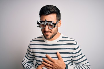 Obraz premium Young handsome man with beard wearing optometry glasses over isolated white background with hand on stomach because indigestion, painful illness feeling unwell. Ache concept.
