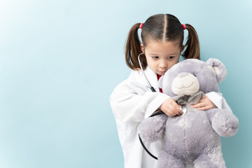 Pretty little girl with ponytails pretend playing as a doctor and checking up her teddy bear with a...