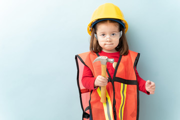 Beautiful little girl aspiring to work in construction and wearing a helmet and a vest and using a hammer