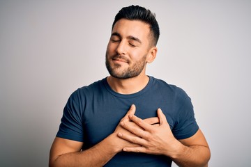 Young handsome man wearing casual t-shirt standing over isolated white background smiling with hands on chest with closed eyes and grateful gesture on face. Health concept. - Powered by Adobe