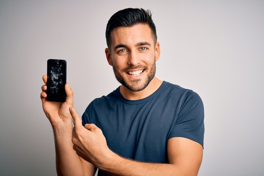 Young handsome man holding broken and cracked smartphone screen over isolated background very happy pointing with hand and finger