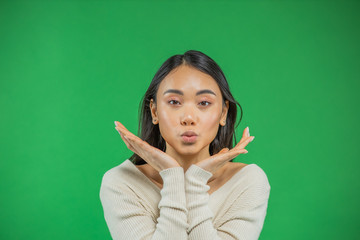 On an isolated green background photo young asian woman with excited dark hair holding face with palms raised, excitedly looking at camera while standing in white blouse