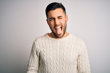 Young handsome man wearing casual sweater standing over isolated white background sticking tongue out happy with funny expression. Emotion concept.