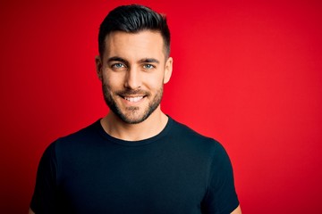 Young handsome man wearing casual black t-shirt standing over isolated red background with a happy...