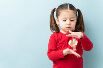 Serious looking little girl looking at a sand timer while practicing self-control during timeout in a studio with copy space