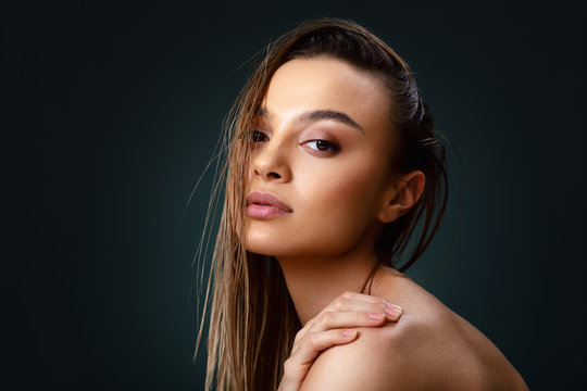 Closeup portrait of beautiful young woman with nice and clean skin with subtle makeup and wet hair on a dark background