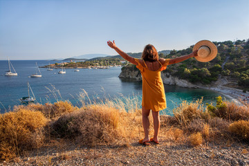 Kastos island happy young woman in a yellow dress and a straw hat enjoying scenic view of the amazing summer seascape with calm sea, anchored sailboats, beautiful nature - Ionian sea, Greece. © VictoriaKurylo