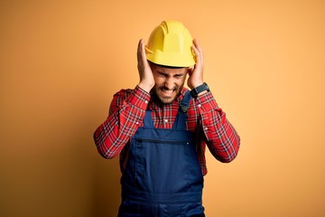 Young builder man wearing construction uniform and safety helmet over yellow isolated background...