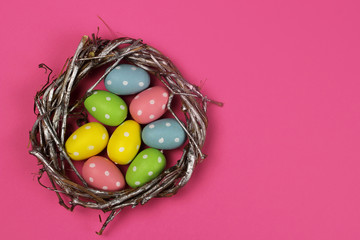 Colored Easter eggs in a nest on a pink background and the