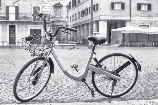 Black and white photo of a bicycle ready for sharing on the empty Navona Square in Rome. Italy. All potential trademarks are removed.