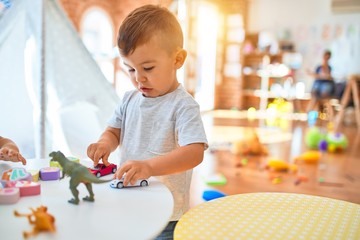 Adorable toddler smiling happy. Standing playing around lots of toys at kindergarten