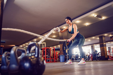 Fototapeta na wymiar Caucasian fit woman dressed in sportsoutfit working hard with battle ropes at gym.