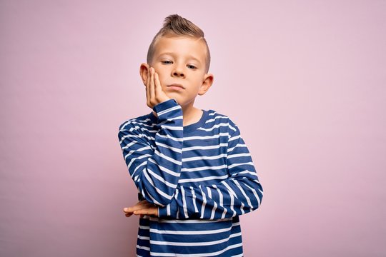 Young little caucasian kid with blue eyes wearing nautical striped shirt over pink background thinking looking tired and bored with depression problems with crossed arms.