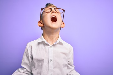 Fototapeta premium Young little caucasian kid with blue eyes wearing glasses and white shirt over purple background crazy and mad shouting and yelling with aggressive expression and arms raised. Frustration concept.