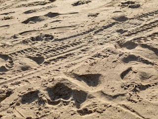 Tire marks and footprints on sandy beach, creating abstract, textured background