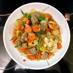 Bowl of stew with beef, carrots, beans, peppers, and potatoes, served in white dish on dark background