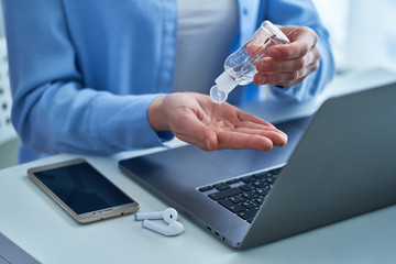 Woman applying an antibacterial antiseptic gel for disinfection and cleaning hands while working at a computer. Protection against viruses, germs and bacteria during coronavirus outbreak