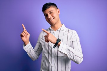 Young handsome hispanic man wearing elegant business shirt standing over purple background smiling and looking at the camera pointing with two hands and fingers to the side.