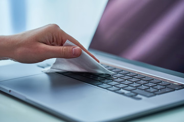 Worker disinfects and cleans working keyboard with antibacterial wet wipes to protect from viruses,...