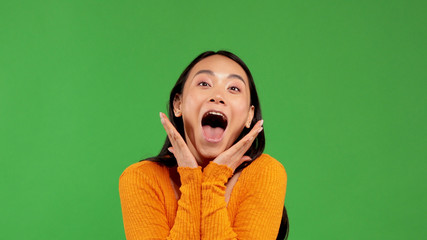 Cheerful cry of young asian woman in bright blouse holds her hands near face without touching face