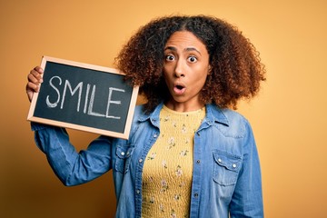 Young african american woman with afro hair holding blackboard with smile message scared in shock with a surprise face, afraid and excited with fear expression