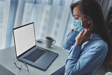 Business woman in a medical protective mask online working from home at the computer during self isolation and quarantine. Coronavirus outbreak, flu epidemic and covid ncov