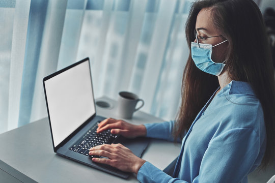 Business woman in glasses and a medical protective mask online working from home at the laptop during self isolation and quarantine. Coronavirus outbreak, flu epidemic and covid ncov novel