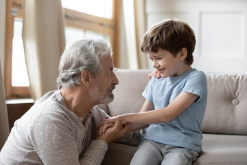 Loving elderly grandfather talk make peace with smiling little preschooler grandson, caring senior grandparent reconcile after fight with cute small grandchild, enjoy time together, bonding concept
