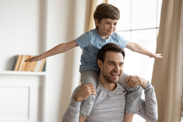 Happy young father carry on back have fun feel playful with little preschooler son at home, smiling...