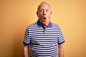 Grey haired senior man wearing casual navy striped t-shirt standing over yellow background afraid and shocked with surprise expression, fear and excited face.