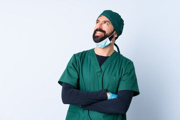 Surgeon man in green uniform over isolated background looking up while smiling