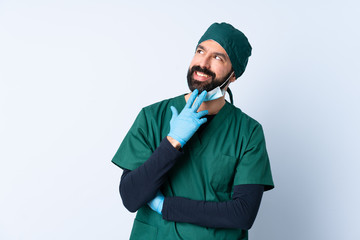 Surgeon man in green uniform over isolated background looking up while smiling