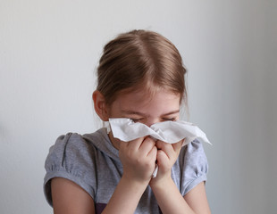 Young girl sneezing into a paper handkerchief in front of a white background.