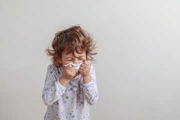 Young girl sneezing into a paper handkerchief in front of a white background.