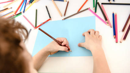 Top view of a boy kid hands who is painting on a blue paper