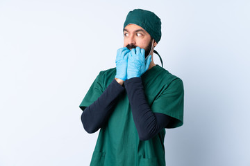 Surgeon man in green uniform over isolated background nervous and scared putting hands to mouth