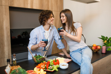 Beautiful couple is smiling while drinking red wine and cooking together in the kitchen