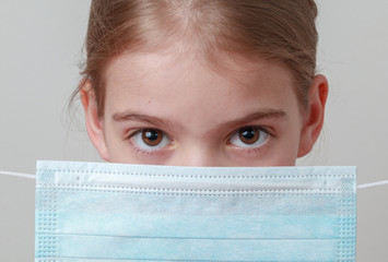 Close-up of a young girl holding a medical mask, symbolizing protection from germs and looking seriously.