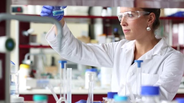 Researcher carrying out scientific experiment in a hi-tech chemistry laboratory. Analyzing results, sampling, pipet, mixing liquids in flasks. 