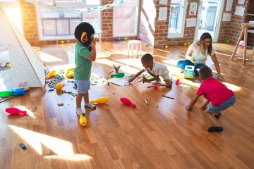Young beautiful teacher and toddlers playing around lots of toys at kindergarten