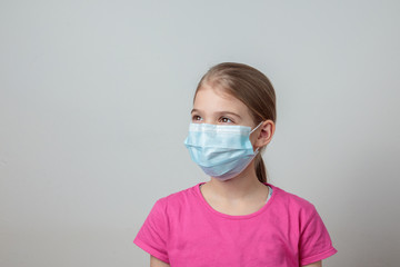 Young girl protecting herself with a medical mask from germs and looking seriously to the side in front of a white background.