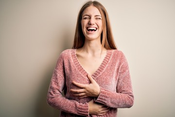 Obraz premium Young beautiful redhead woman wearing pink casual sweater over isolated white background smiling and laughing hard out loud because funny crazy joke with hands on body.