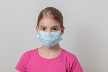 Young girl protecting herself with a medical mask from germs and looking seriously in front of a white background.