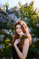 Naklejka premium Portrait of woman holding lilac flowers bouquet on blossomig bush background