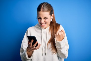 Fototapeta premium Young redhead sportswoman doing sport listening to music using earphones and smartphone very happy and excited doing winner gesture with arms raised, smiling and screaming for success. Celebration