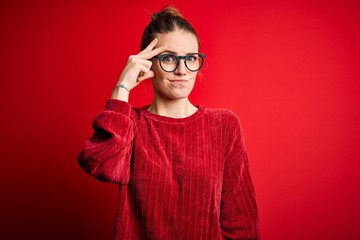 Young beautiful redhead woman wearing casual sweater over isolated red background worried and stressed about a problem with hand on forehead, nervous and anxious for crisis