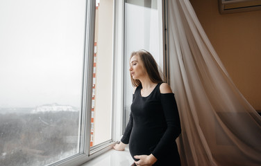 A pregnant girl is breathing fresh air from the window