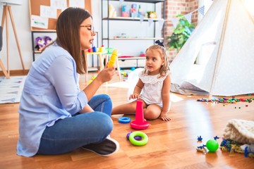 Caucasian girl kid playing and learning at playschool with female teacher. Mother and daughter at playroom playing with inteligence toys