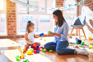 Caucasian girl kid playing and learning at playschool with female teacher. Mother and daughter at playroom around toys playing with bulding blocks