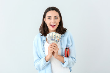 Young woman with wallet and money on light background